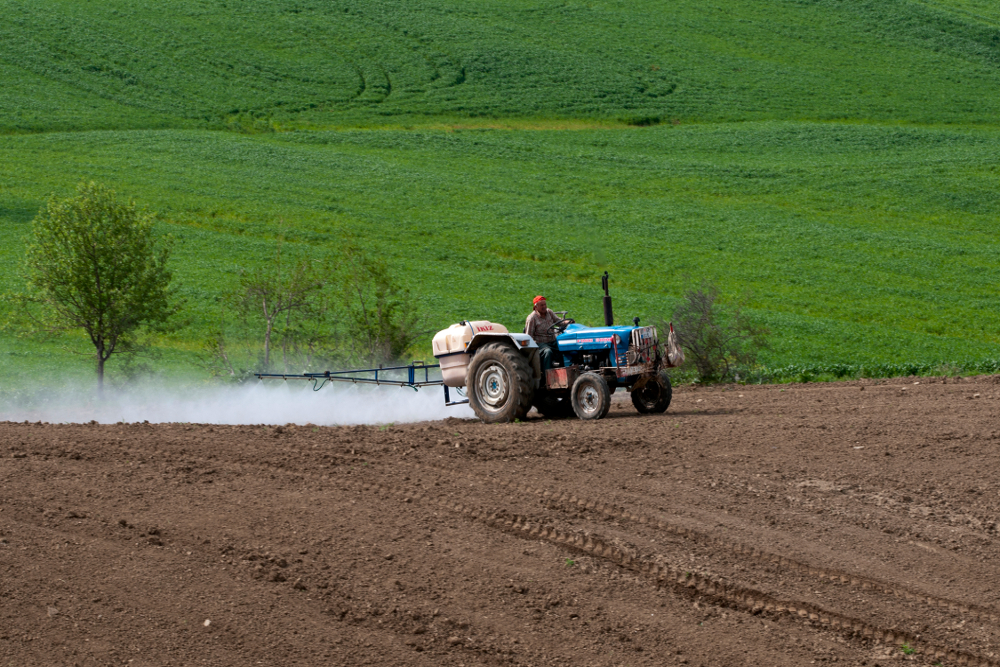 Farm tractor spreading chemical onto farmland in preparation for planting
