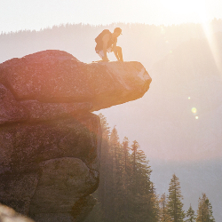 Man climbing large cliff face in bright sunlight
