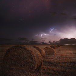 Lightning storm rising over hay bales on a farm field