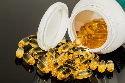 Vitamin capsules containing yellow oil falling out of a bottle