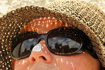 Woman lying in the sand with a hat, sunglasses, and sunblock on her nose