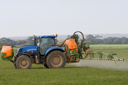 Large blue tractor spraying a field of crops on a farm