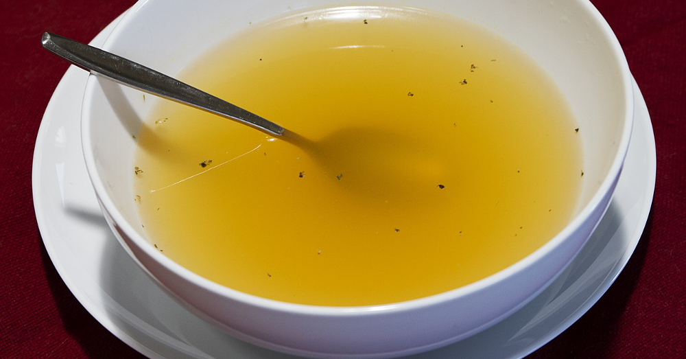 Clear yellow broth in a white bowl with a spoon