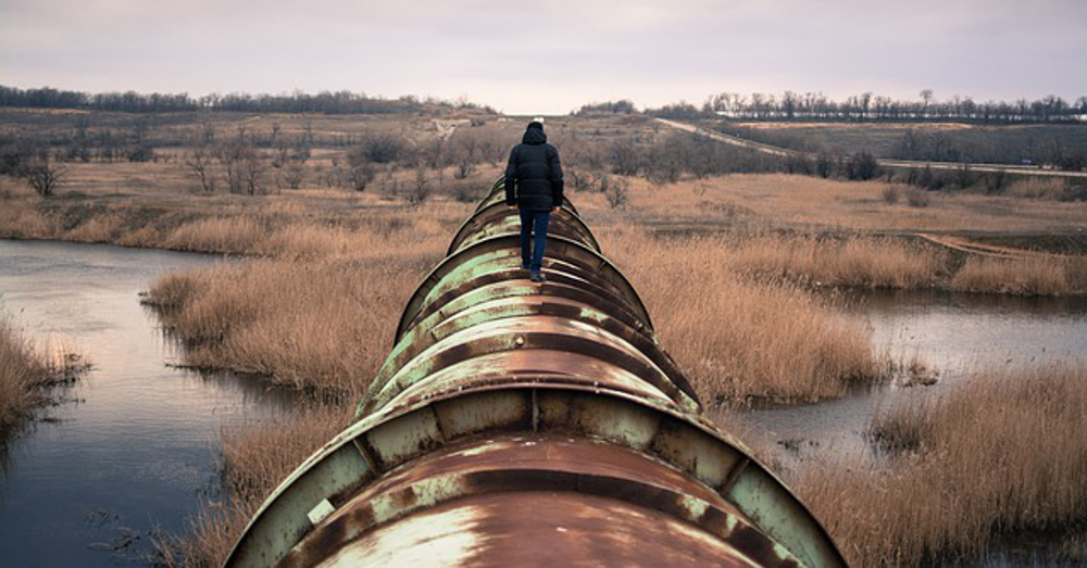 Person walking along a rusted pipeline in a wetland