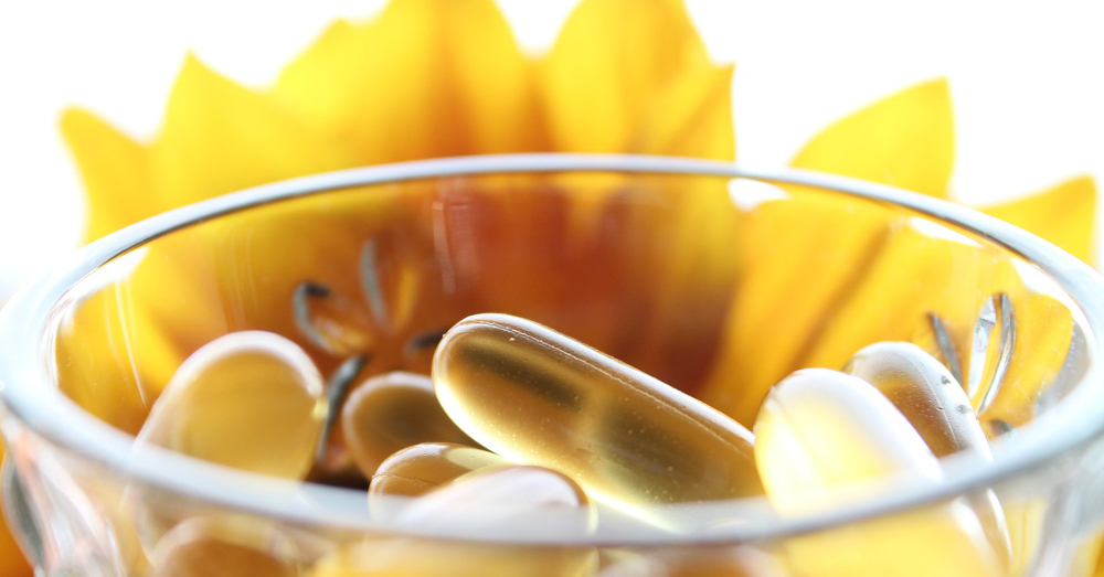 Supplemental vitamins in a glass bowl near a yellow flower