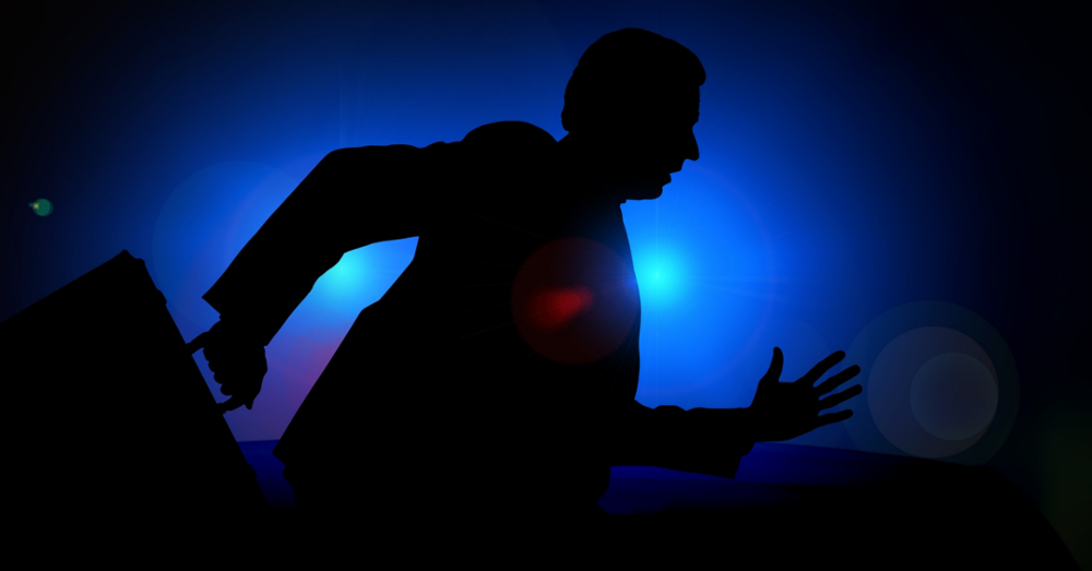 silhouette of a business man running from police car lights