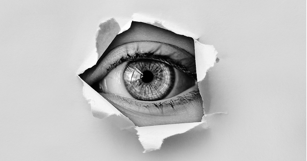 A single eye spying through a torn hole in some paper
