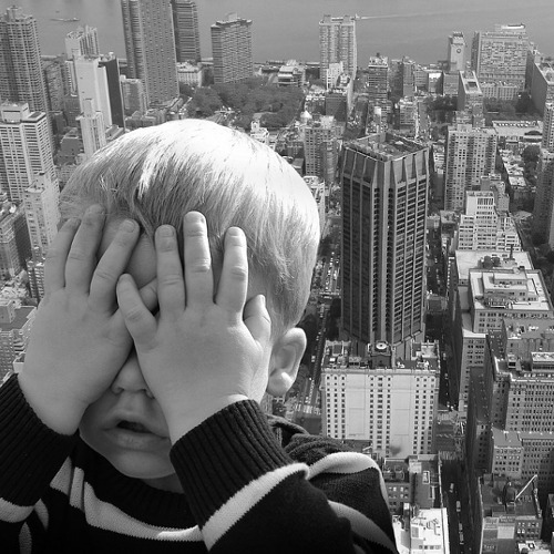 Kid covering eyes overlooking city of buildings