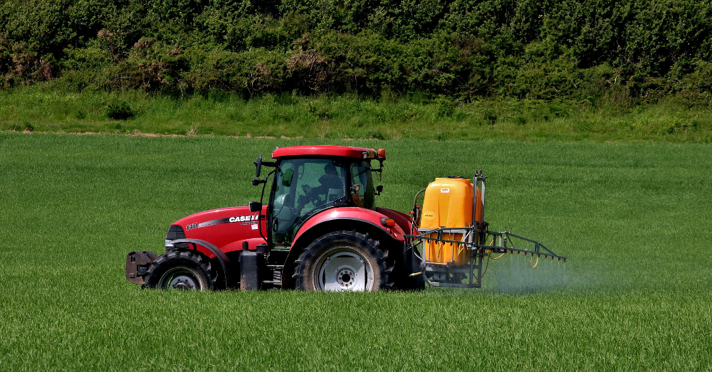 red farm tractor spraying pesticide on crop field