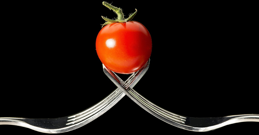 Two forks holding a tomato