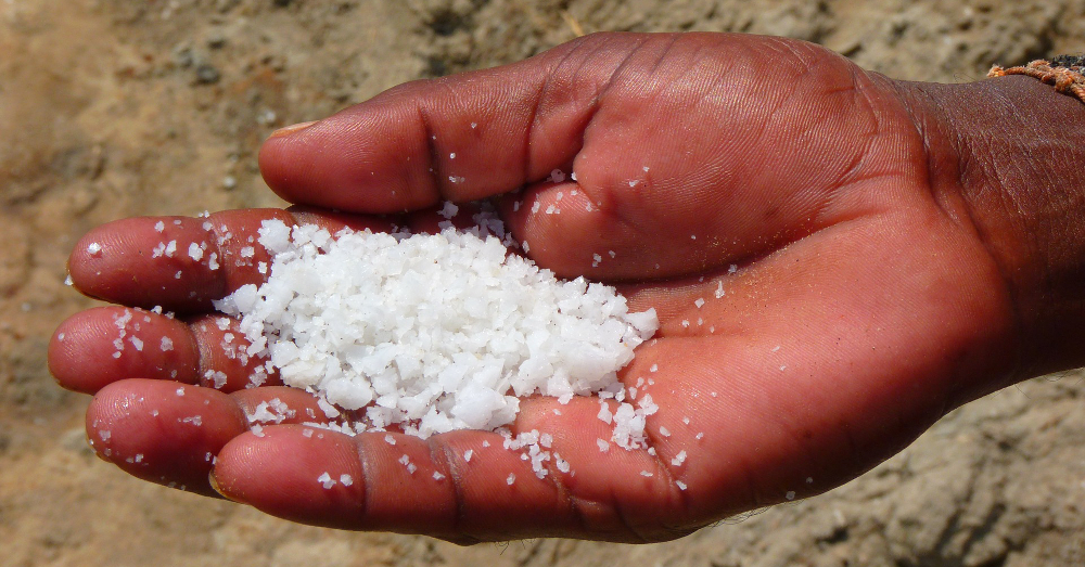 hand holding white salt on a sandy beach