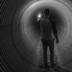 person walking down a large drain tunnel with a flare light