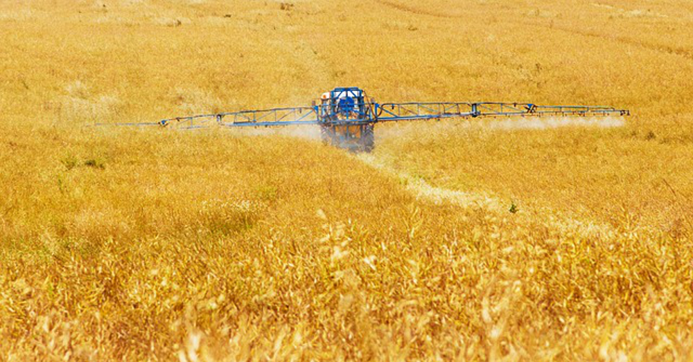 tractor spraying chemical herbicide on crop field at a farm