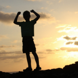 kid standing on rock with hands in air