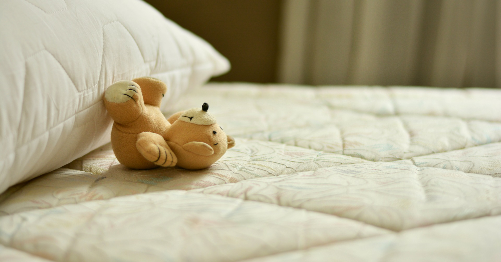 teddy bear laying on a mattress and pillow