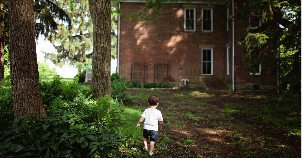boy walking through the woods beside a brick house