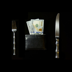 knife and fork surrounding a wallet with cash