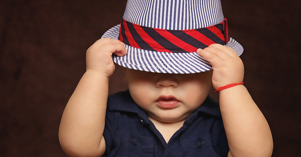 young baby wearing a striped fedora hat over their eyes