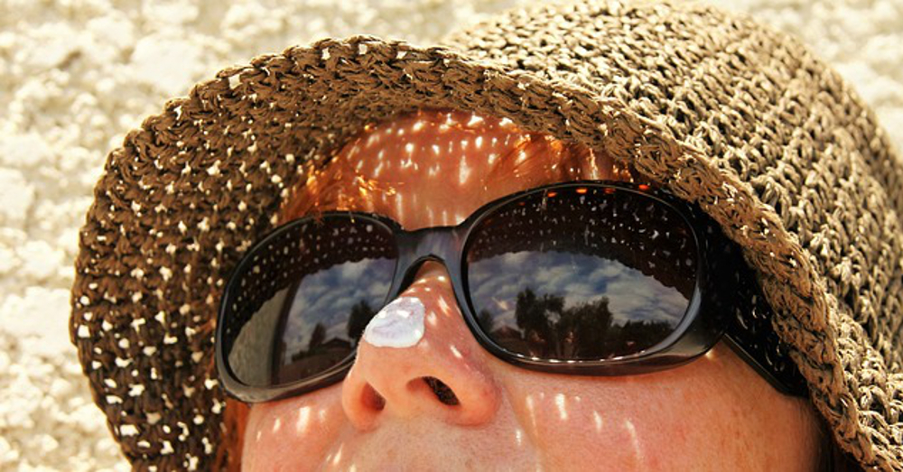 person with sunscreen on nose with hat and sunglasses on the beach