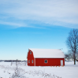 red barn in a farm field during winter covered in snow