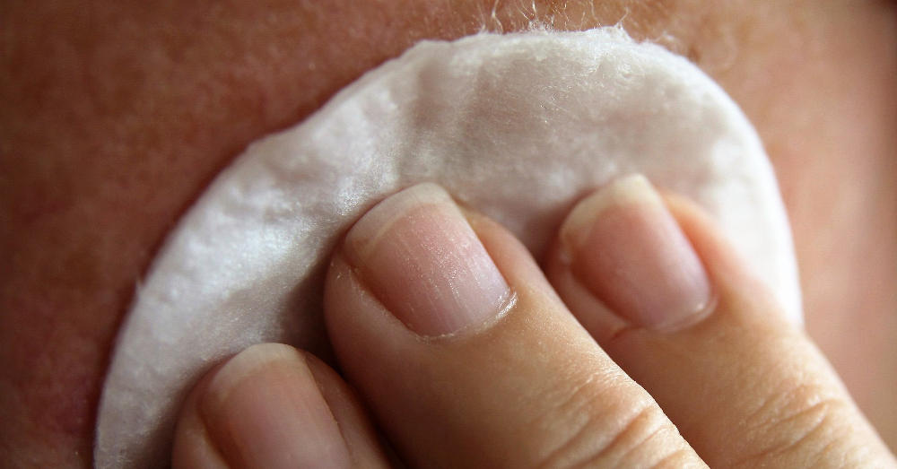 hand with a cotton pad cleaning a face