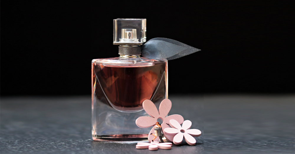 small plastic figures and pink flowers surrounding a glass perfume bottle