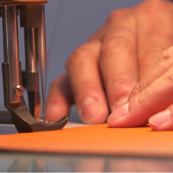 pair of hands using a sewing machine to sew together leather pieces
