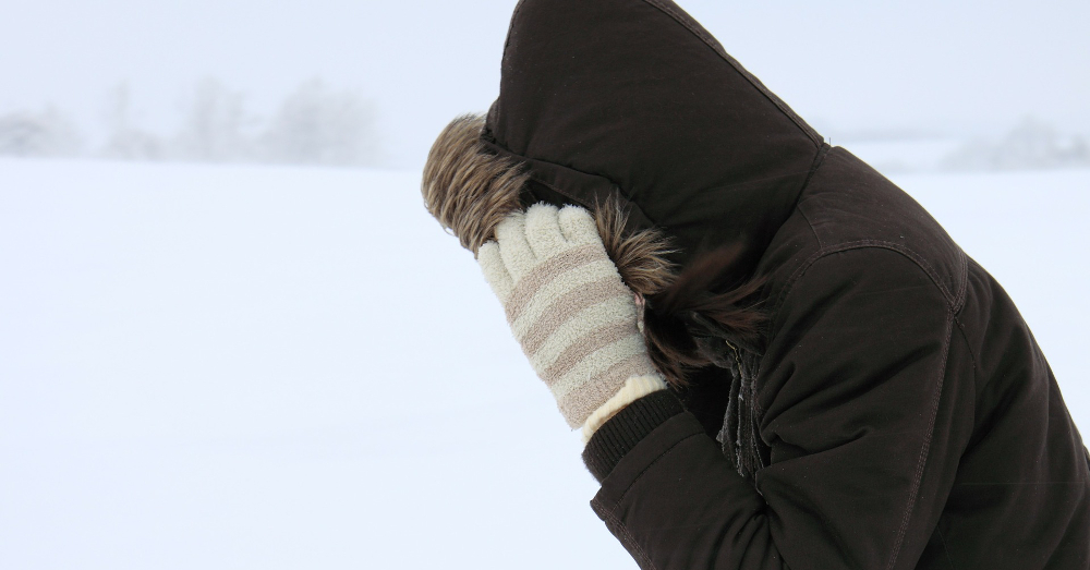 person outside in a blizzard with a furry hood and white striped gloves