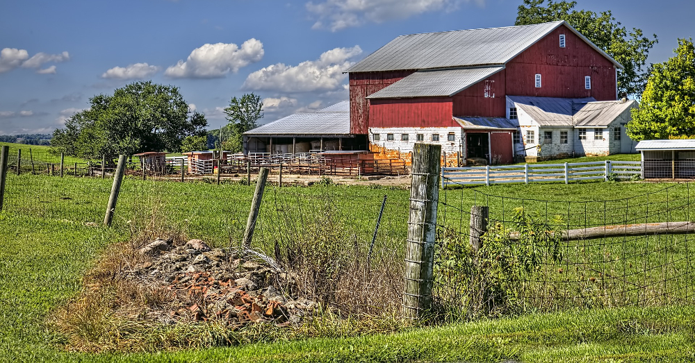rocks and debris beside a fence in a farm field near a red barn