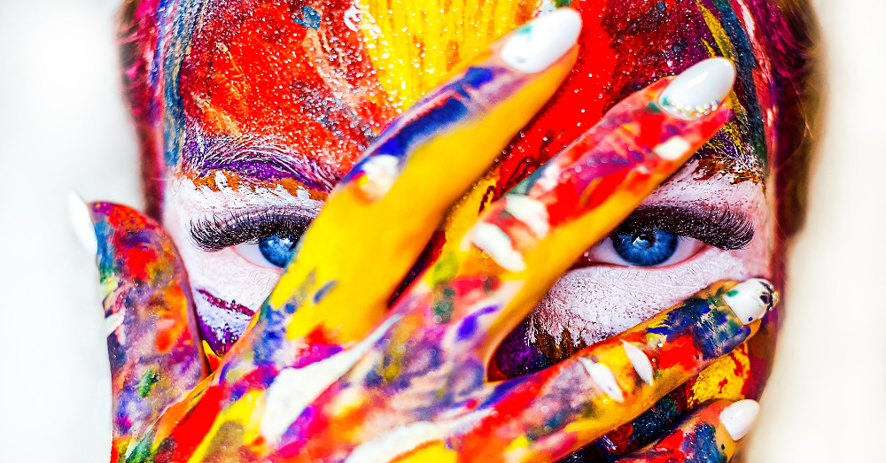 woman with colorful paint for makeup covering her face with her hand