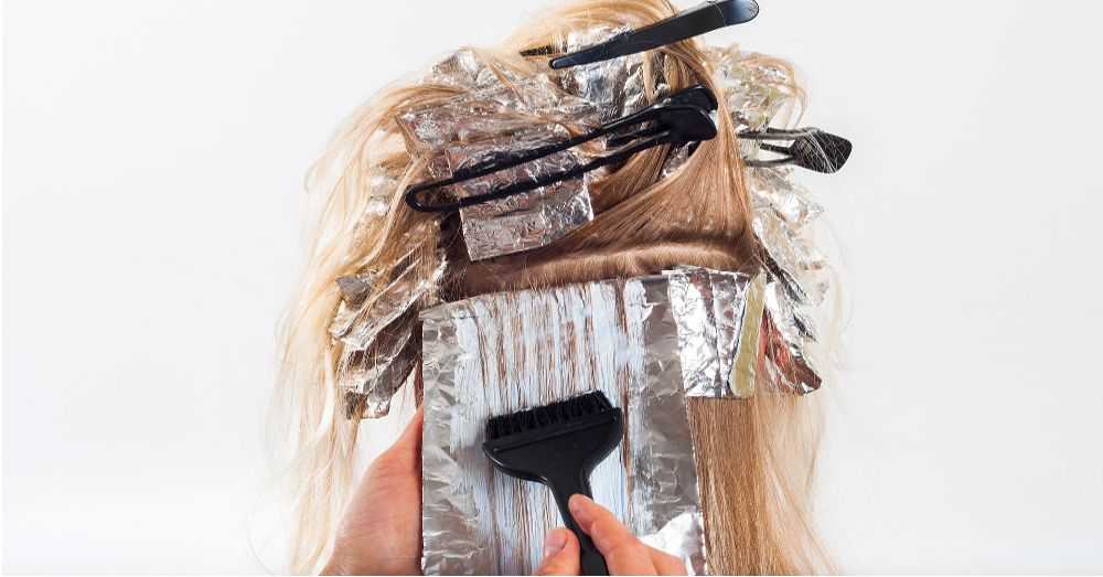 hairdresser in a salon coloring a womans hair with foil and a brush