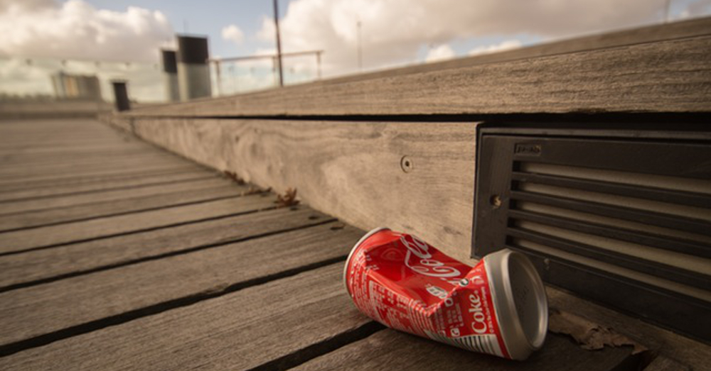 crushed coca cola soda pop can on a wooden boardwalk in the sun