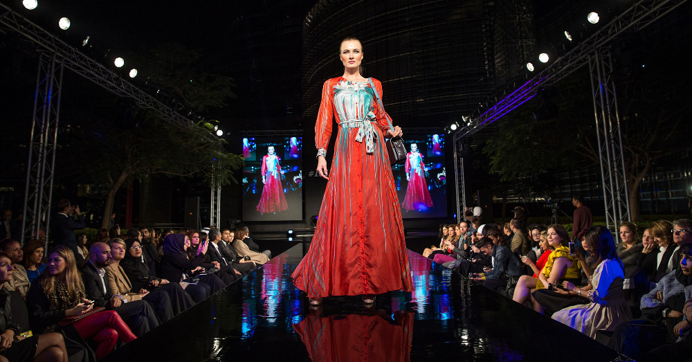 model dressed in a red gown walking down a runway at a fashion show