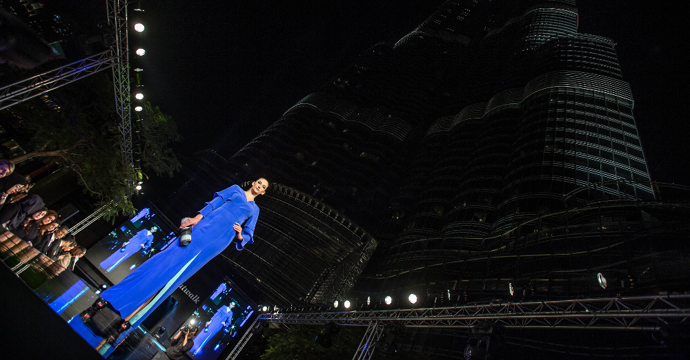 model walking a catwalk runway in front of a skyscraper at night during a fashion show
