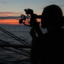 person navigating with a sextant on a ship in the ocean at sunset