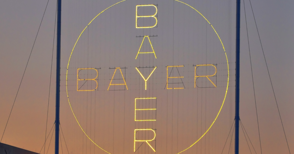 Bayer logo in neon lights above a warehouse at sunset