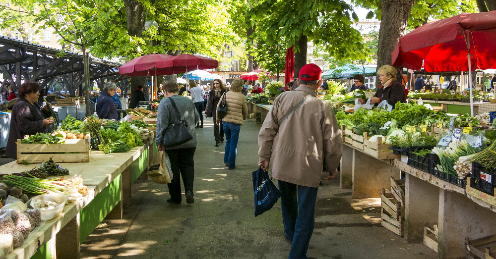 people walking down a line of farmers market stalls selling produce