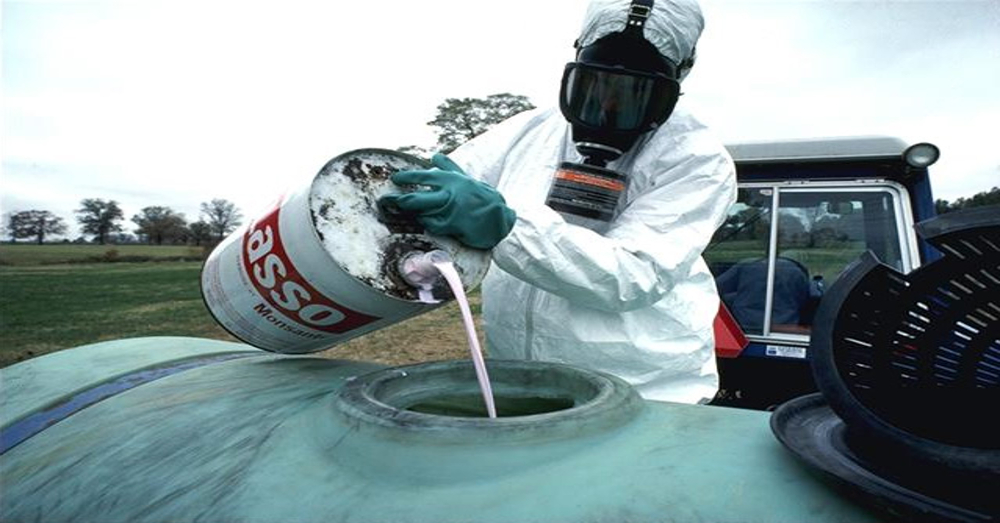 person in hazardous material suit and mask pouring toxic chemicals into a large metal tank