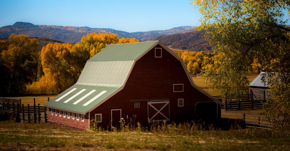 red barn building on a farm field in a mountain landscape at sunset