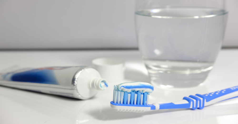 toothbrush with blue and white toothpaste in a white tiled bathroom near a glass of water