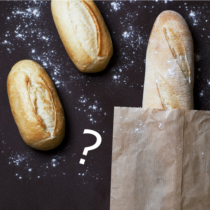 assorted loaves of bread with bits of flour and a paper bag with a question mark