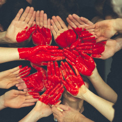 hands coming together with red paint in the shape of a heart