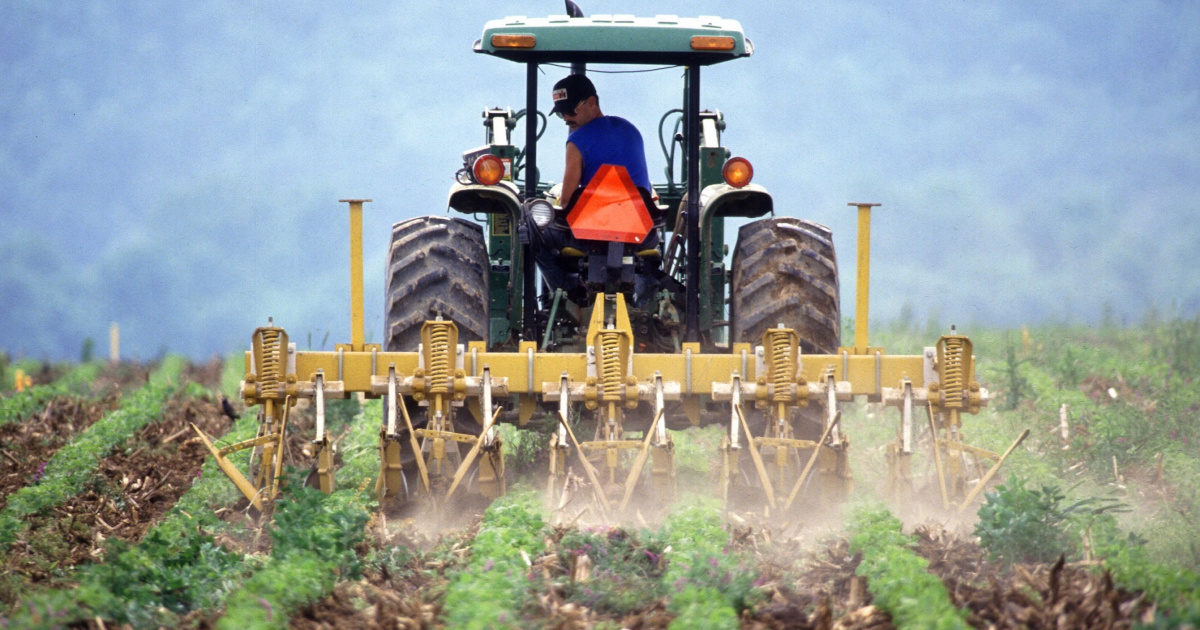 farmer on a tractor spraying a crop field with pesticide or herbicide