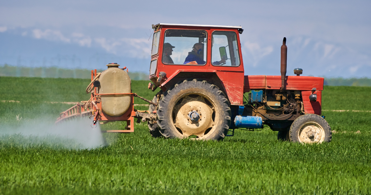 red tractor on a farm crop field spraying a pesticide mist