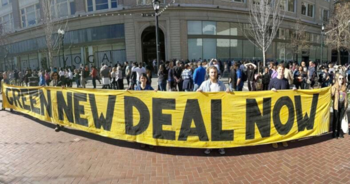 several people holding a large yellow sign with black letters stating GREEN NEW DEAL NOW
