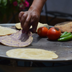 person making tortillas on a wood fire grill with tomatoes and peppers