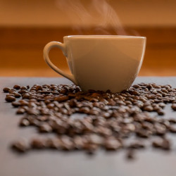 steaming cup of coffee surrounded by roasted coffee beans