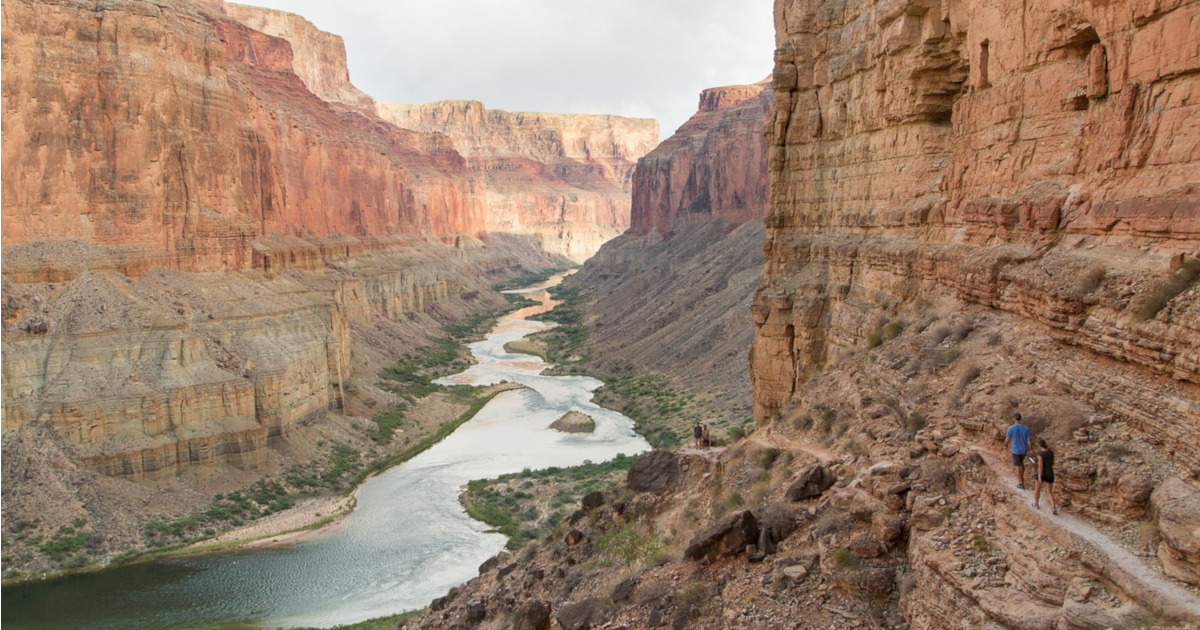 two hikers walking along a canyon path near the Colorado River on a sunny day