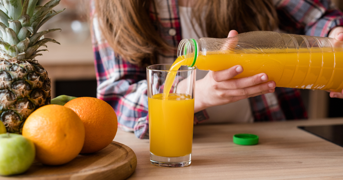 woman pouring orange juice into a glass in a kitchen by fresh fruit
