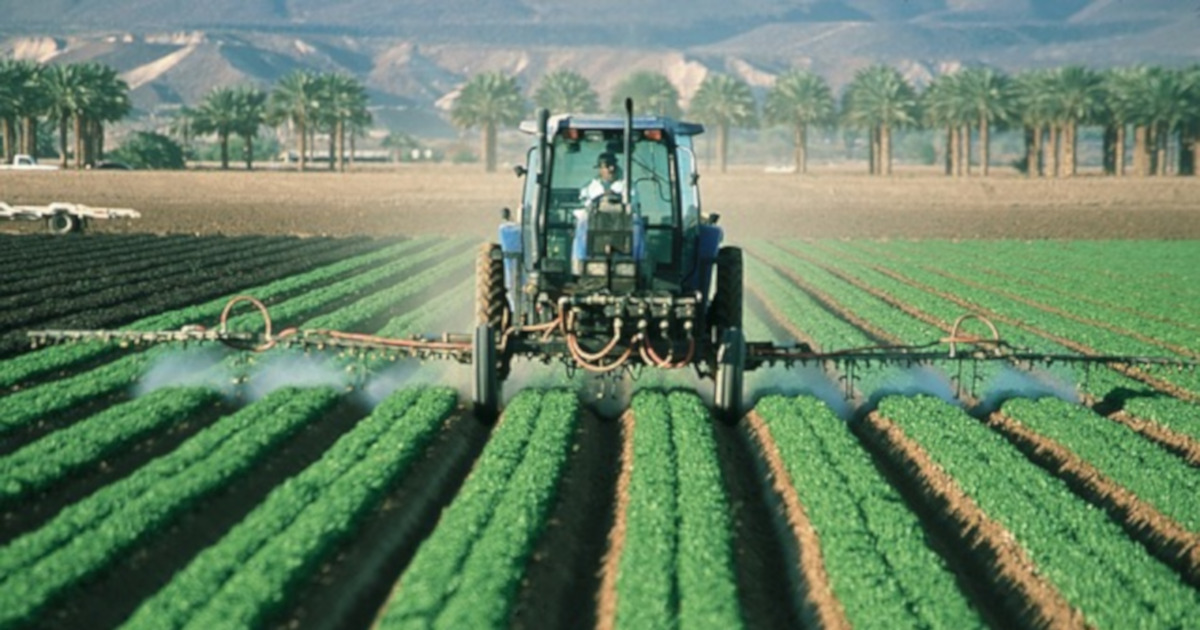 farmer in a tractor spraying a crop field with pesticides